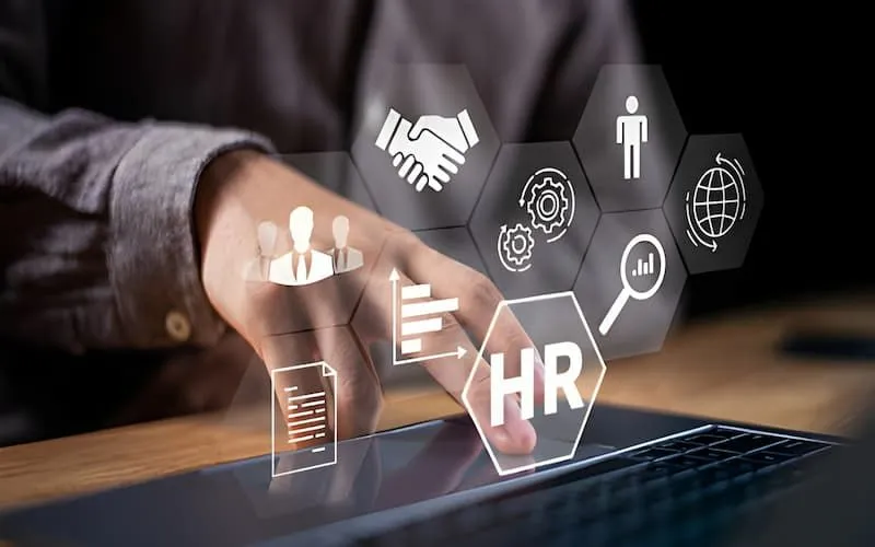Hand interacting with a laptop showing a digital overlay of HR icons including handshake, gears, HR document, and global network